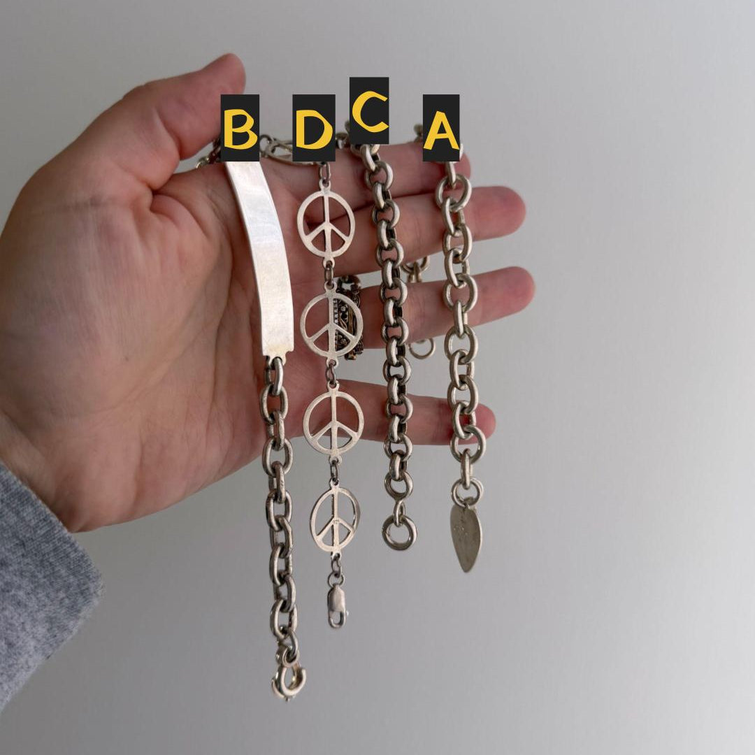 Hand holding a set of chains with peace symbol charms and labeled 'B D C A' on a plain background.